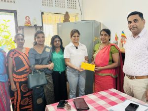 A photo of the president of the HCK PPA surrounded by a few PPA committee members and the staff members of Wathuliyadda Primary School, handing over the donation to the Principal of Whathuliyadda Primary School.